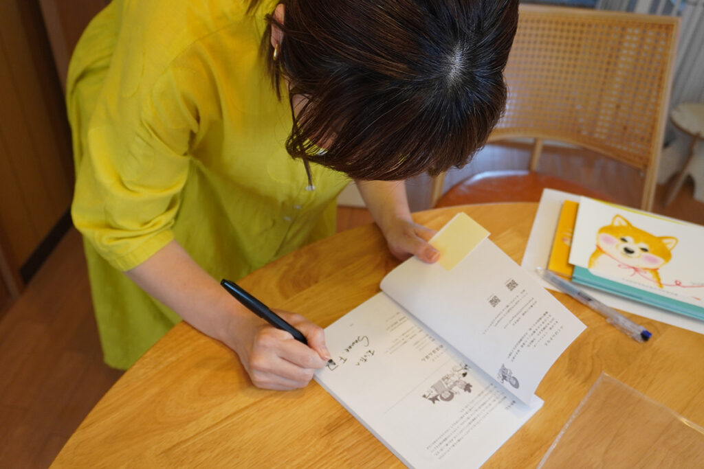 単行本『のほほんほん』に心を込めてサインを描いてくださるふくはらさなえさん。愛犬「むった」の名前もかわいく添えていただき、宝物の一冊になりました!